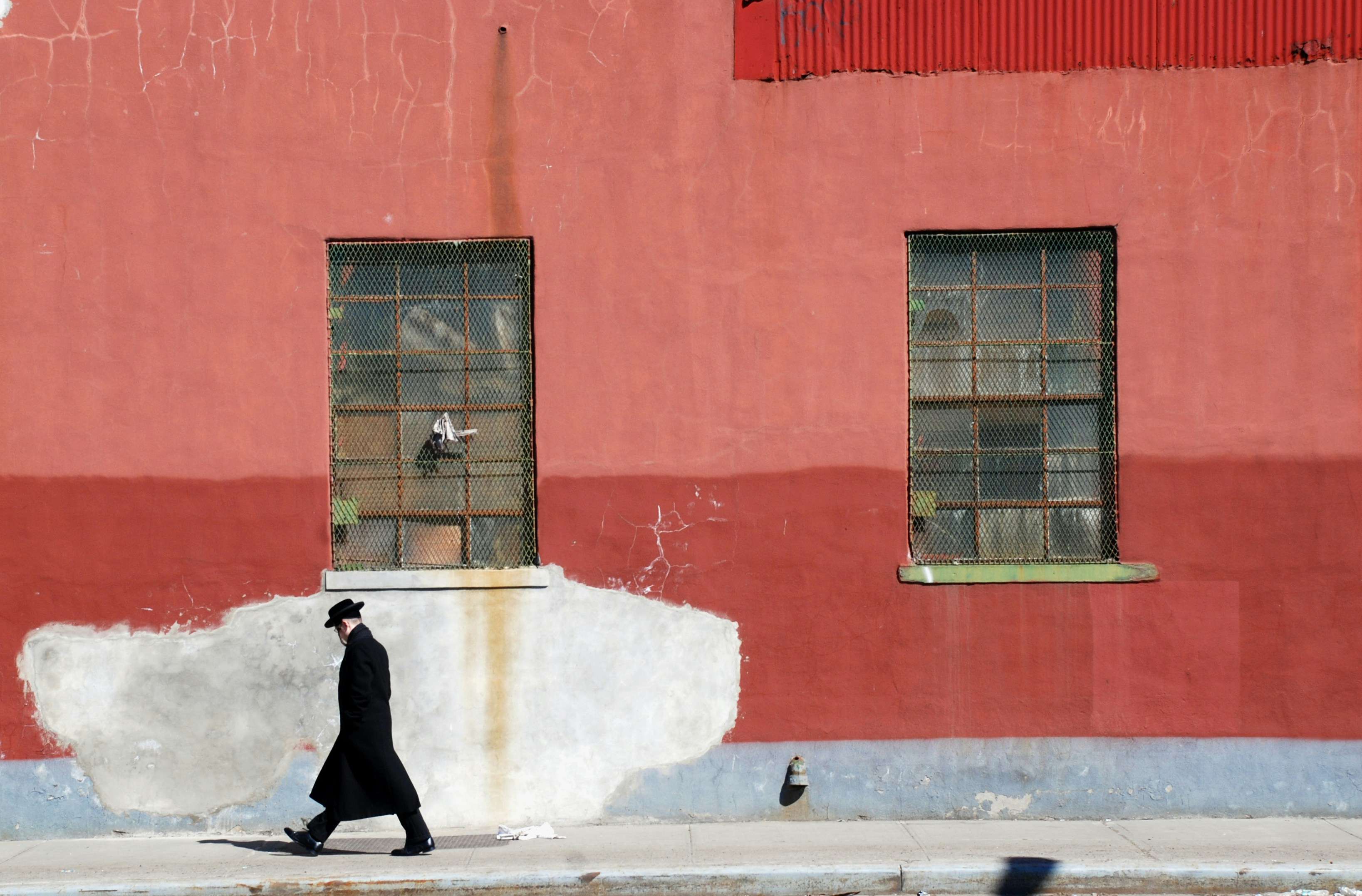 A Jewish man walking down a sidewalk in front of a red building