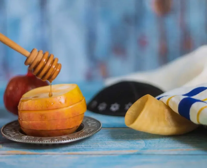 A honey stick with honey dripping onto a sliced apple.